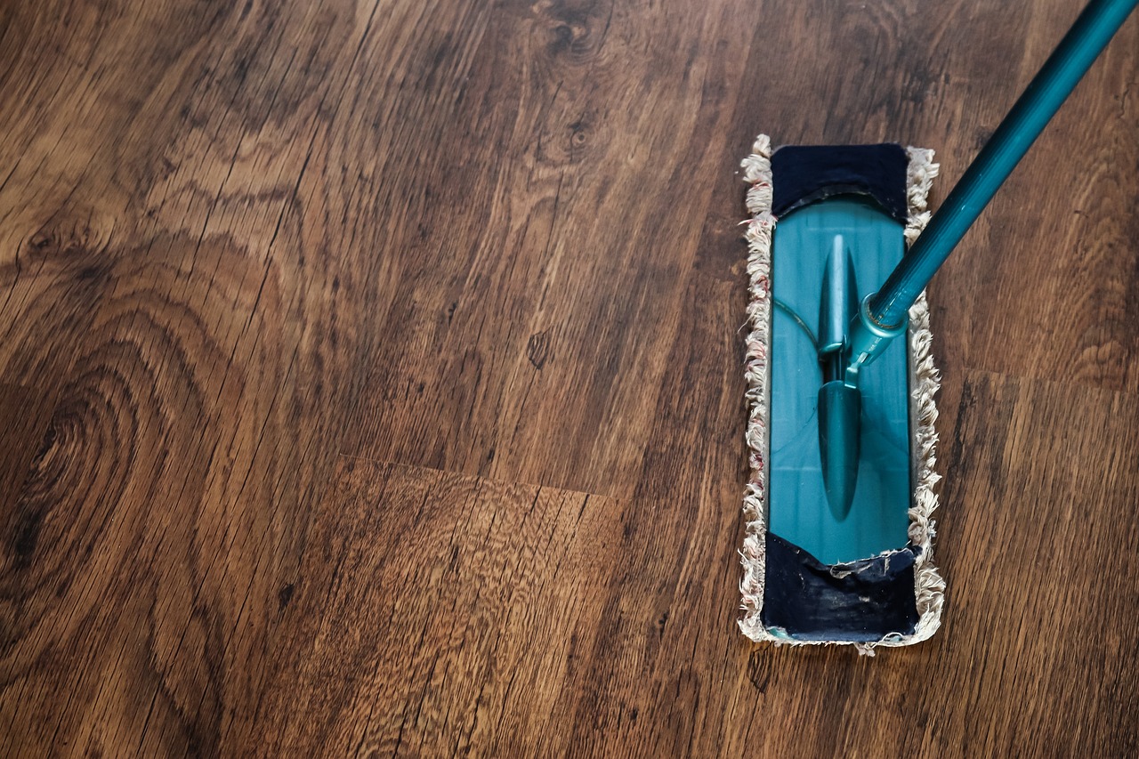 Dunkler Parkettboden in braun, und eine Wischmop in blau. Bodenreinigung währen einer Gebäudereinigung,