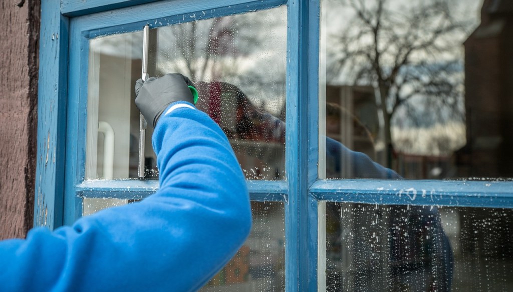 Ein Fenster mit blauem Rahmen, wird bereinigen, ein Arm mit blauer Jacke und schwarzen Handschuhen. Das Beispiel einer professionellen Fensterreinigung.